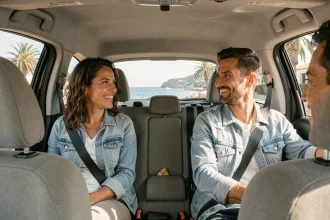 Trois adultes pratiquant le covoiturage sur la Côte d'Azur, souriant dans une voiture compacte avec vue sur le littoral méditerranéen